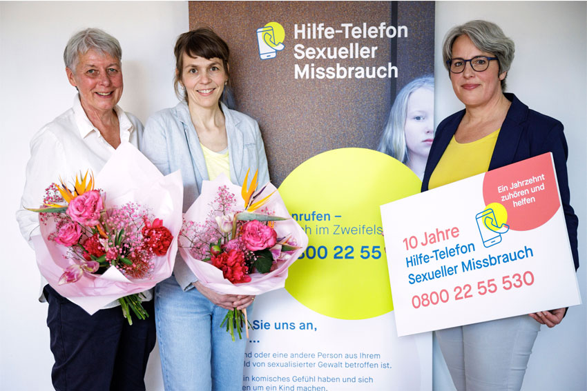 Ein Gruppenfoto mit Silke Noack, Tanja von Bodelschwingh, Kerstin Claus vor einem Aufsteller "10 Jahre Hilfe-Telefon Sexueller Missbrauch".