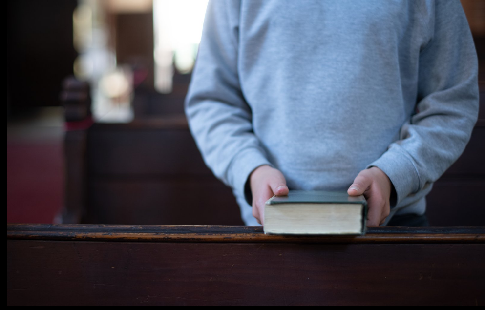 Person mit einer Bibel in der Hand steht vor einer Kirchenbank