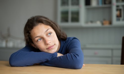 Ein Mädchen lehnt mit verschränkten Armen auf dem Esstisch und blickt nachdenklich in die Ferne