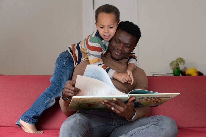 Vater und Sohn auf dem Sofa, der Vater liest ein Bilderbuch vor