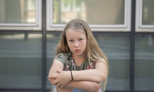 Ein Mädchen sitzt im T-Shirt vor einem Fenster und blickt in die Kamera