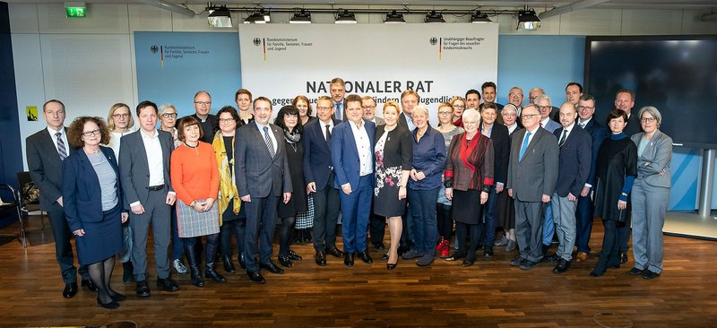 Das Foto zeigt 36 Mitglieder des Nationalen Rats gegen sexuelle Gewalt an Kinder und Jugendlichen beim gemeinsamen Fototermin anlässlich einer Sitzung. Die Vertreter:innen stehen vor einer weißen Fotowand des Nationalen Rats.