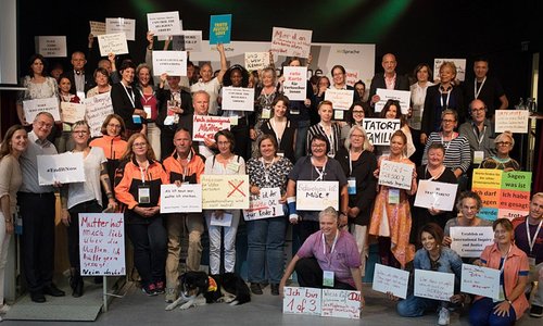 Das Foto zeigt ein Gruppenbild von Teilnehmenden des Kongresses "MitSprache" im Jahr 2018. Die Personen präsentieren Schilder und Plakate, auf die sie Botschaften geschrieben haben.