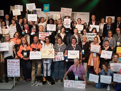 Das Foto zeigt ein Gruppenbild von Teilnehmenden des Kongresses "MitSprache" im Jahr 2018. Die Personen präsentieren Schilder und Plakate, auf die sie Botschaften geschrieben haben.