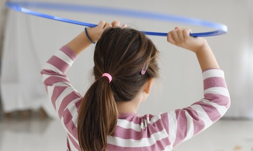 Das Foto zeigt ein Mädchen, das mit einem Hula-Hoop-Reifen spielt. Die Szene ist von hinten aufgenommen, das Gesicht des Mädchens ist von uns abgewandt.