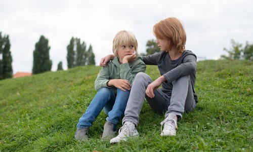 Zwei Jungen sitzen auf einer Wiese, der Ältere legt den Arm um den Jüngeren