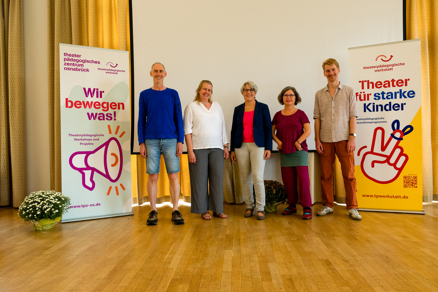 Fünf Menschen stehen auf einer Bühne neben zwei Schauwänden der Theaterpädagogischen Werkstatt